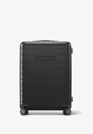 Valise rigide noire avec un design à rainures horizontales, une poignée supérieure et deux roues. Comprend un emplacement pour une carte d'identité encastré à l'arrière.