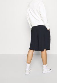 Sudadera blanca con puños acanalados combinada con una falda negra hasta la rodilla, con bolsillos y un corte relajado, llevada con zapatillas blancas.