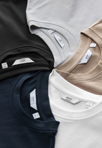 Five folded crewneck t-shirts in black, navy, white, beige, and gray with visible "NEXT Relaxed Fit" size tags.