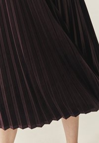 Donker bordeauxkleurige geplooide rok van zachte fluwelen stof, met een uitlopende design en een zoom met een zigzagpatroon.