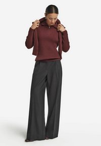 Bordeaux rille strikpullover med halvlukket krave, parret med brede grå bukser, der viser en kontrast af tekstureret stof.