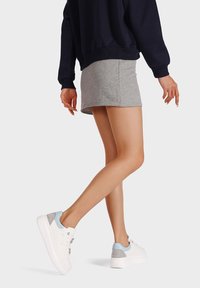 Sneakers bianchi con accenti blu chiaro e grigi, abbinati a una mini gonna grigia e a una felpa oversize blu navy. Il modello è in posa di camminata.