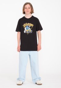 Camiseta de algodón negra con un estampado gráfico colorido que presenta la marca "Volcom", combinada con unos pantalones vaqueros de pierna ancha en azul claro y zapatillas blancas.