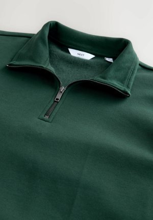 Sudadera de media cremallera verde oscuro con un interior suave, que presenta una cremallera plateada y un cuello acanalado. La tela es lisa y tiene una textura uniforme.