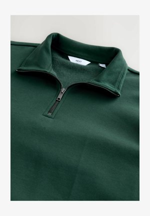 Pullover vert foncé avec fermeture éclair quart zip et intérieur doux, doté d'une fermeture éclair argentée et d'un col côtelé. Le tissu est lisse avec une texture homogène.