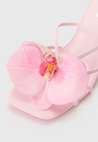 Roze sandalen met een glanzende afwerking, voorzien van een grote, gestructureerde orchidee bloemaccent op de teenband. Dunne, delicate bandjes. Vierkante teenontwerp.