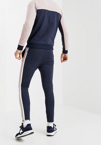 El chándal en navy y rosa presenta un diseño a bloques de color con un corte ajustado, franjas laterales y puños acanalados. El material tiene una textura suave.