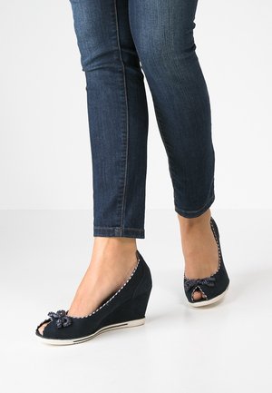 Sandales compensées bleu marine avec un design à bout ouvert, en tissu texturé et ornées de nœuds décoratifs. Elles présentent une semelle et un liseré blancs contrastants.