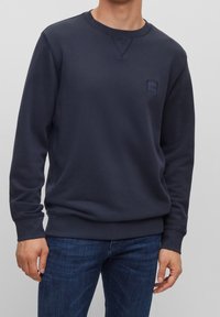 Mörkblå sweatshirt i bomullsblandning, med långa ärmar, ribbade muddar och nederkant, samt en liten logotyp på bröstet.