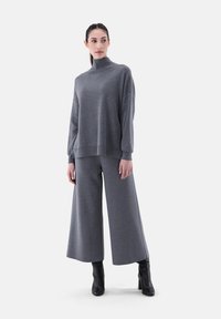 Grauer übergroßer Pullover mit hohem Kragen und weiten Ärmeln, kombiniert mit passenden weit geschnittenen Hosen. Getragen mit Stiefeletten. Weicher Stoff.