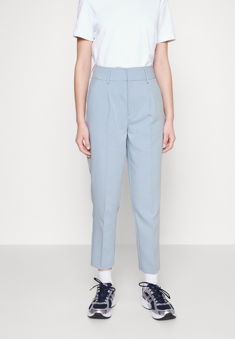 Pantalons bleu clair à coupe ajustée, avec des plis latéraux et un design à jambes droites. Associés à un t-shirt blanc et des sneakers.