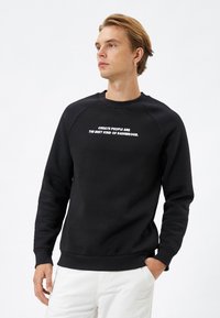 Zwarte sweatshirt met raglanmouwen, ronde hals en ribgebreide boorden. Voorzien van witte tekst: "Geweldige mensen zijn de beste soort gevaarlijk."