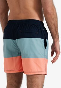 Heren zwembroek met een gestreept ontwerp in marineblauw, lichtblauw en koraal. Elastische tailleband, achterzak en zijzakken zichtbaar.