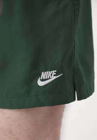 Pantalones cortos de tela verde con un logo de Nike bordado en blanco en el dobladillo inferior y una abertura lateral para facilitar el movimiento.
