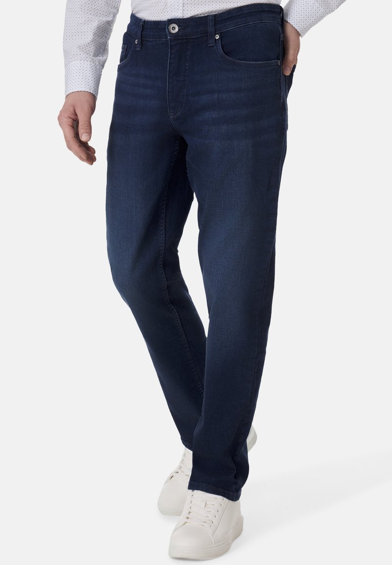 Dunkelblaue Jeans aus Denim mit geradem Schnitt, zwei vorderen Taschen, Reißverschluss und kontrastierenden Nähten. Kombiniert mit weißen Sneakers.