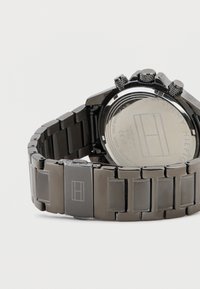 Orologio in acciaio inossidabile con finitura metallica nera, maglie rettangolari e funzione cronografo. Sul retro sono riportati il logo del marchio e le specifiche.