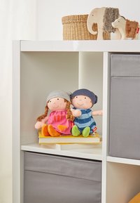 Zwei weiche Stoffpuppen sitzen auf einem Stapel Bücher. Die eine Puppe trägt ein pinkes Kleid und einen grauen Hut, die andere ein blau gestreiftes Hemd und einen dunklen Hut.