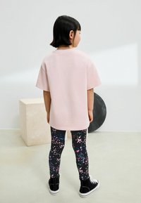 Ljusrosa överdimensionerad t-shirt som matchas med svarta leggings med ett flerfärgat splattermönster. Svarta högsneakers fullbordar looken.