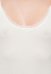 Weißes, geripptes Tanktop mit V-Ausschnitt, verziert mit zarter Spitzenborte, aus einem weichen, strukturierten Strickstoff.