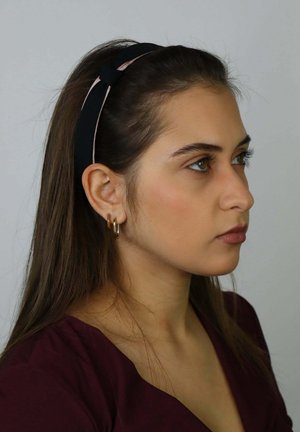 Zwart en roze stoffen haarband met knoopdetail, gedragen op lang bruin haar, met gouden oorringen en een wijnroze top.