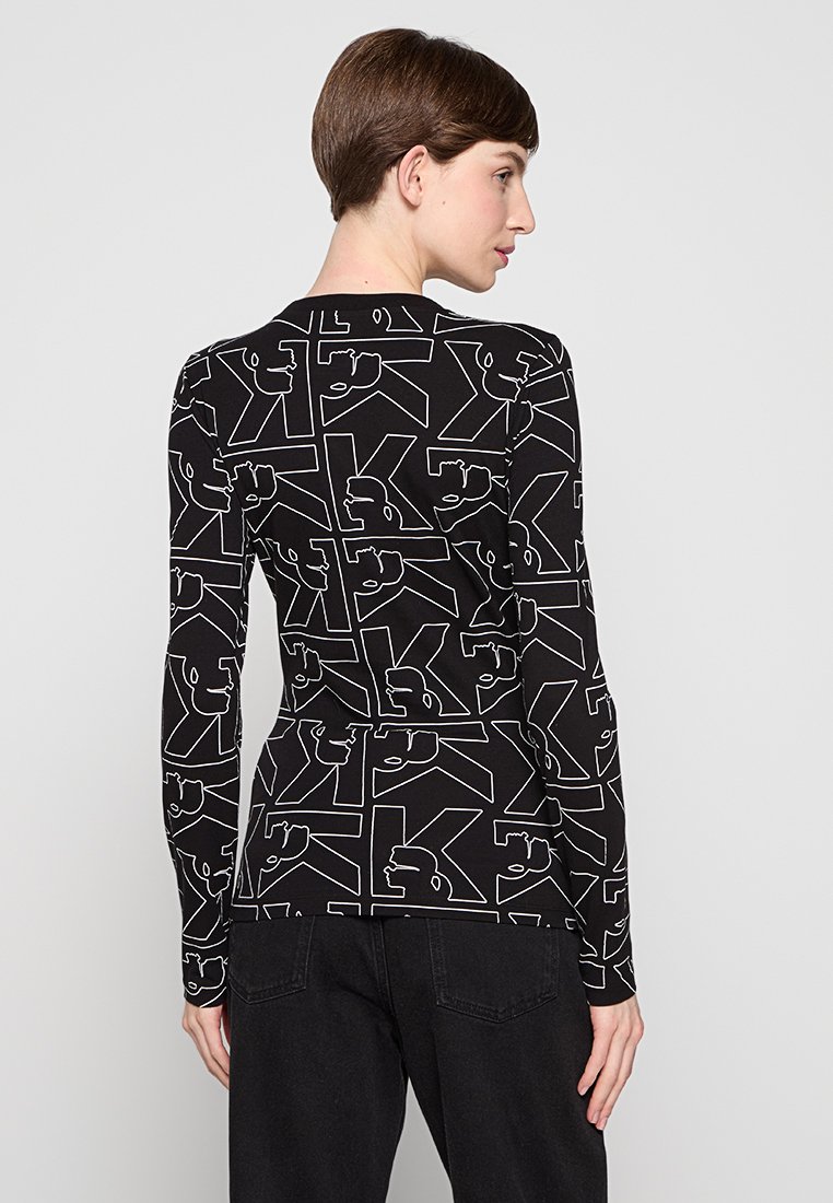 Maglietta a maniche lunghe realizzata in un tessuto nero elastico con motivi grafici astratti bianchi. Design aderente con scollatura a girocollo.