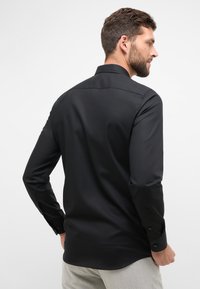 Schwarzes Langarmshirt aus glattem Stoff mit klassischem Kragen und Knopfmanschetten, mit taillierter Passform und abgerundetem Saum.
