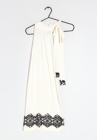 Robe blanche sans manches avec un détail de l'épaule noué, présentant des accents en dentelle noire le long de l'ourlet dans un motif géométrique.