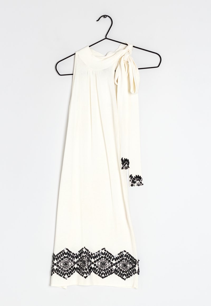 Robe blanche sans manches avec un détail de l'épaule noué, présentant des accents en dentelle noire le long de l'ourlet dans un motif géométrique.