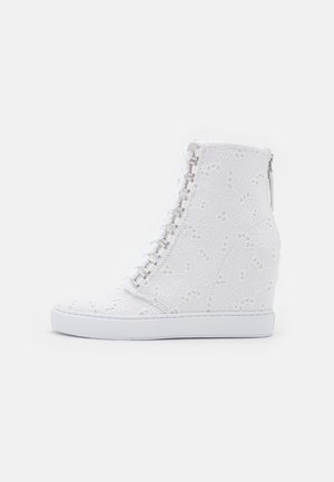 Baskets compensées blanches avec motif de dentelle florale, lacets à l'avant et fermeture éclair à l'arrière sur fond uni.