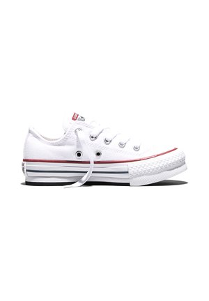 Zapatilla blanca de lona baja con cordones blancos, rayas rojas y negras en la suela de goma y ojales metálicos sobre un fondo blanco.