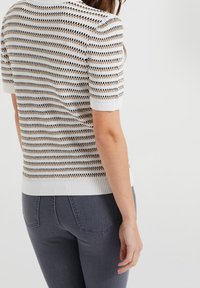 Top de punto de manga corta con base blanca, con rayas horizontales en negro y dorado. Textura suave y puños acanalados en las mangas.