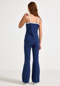 Marineblaue Schlaghose und passendes Tanktop mit hellblauem Saum. Glatter Stoff, figurbetontes Design und verstellbare Träger.