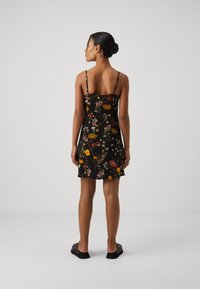 Svart ermeløs kjole med blomstermønster i rødt, gult og grønt. Lett stoff, tettsittende design og justerbare tynne stropper.