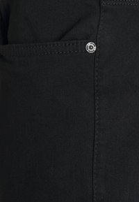 Material de denim negru cu o textură netedă, având un detaliu cu un nasture argintiu pe buzunarul lateral și cusături contrastante de-a lungul cozilor.