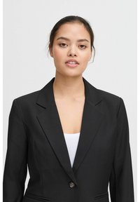 Černý blazer s klopovým límcem, na jediné knoflíkové zapínání a dvěma předními kapsami. Hladká tkanina se strukturovaným střihem, seštílený design.