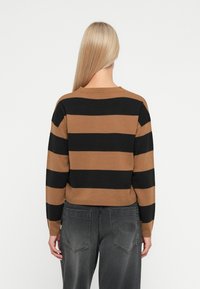 Brown and black striped knit sweater with a crew neckline, ribbed hem, and long sleeves. Worn with dark gray loose-fitting jeans.