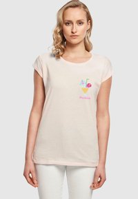 Lys rosa bomull t-skjorte med korte rullede ermer, som har et brodert drikkeillustrasjon med et sugerør, paraply og blomst detaljer.