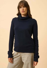 Marineblauer Strickpullover mit einem weiten Stehkragen und langen Ärmeln. Weicher Textur, tailliert und kombiniert mit hellen, weit geschnittenen Hosen.