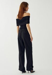 Čierny top bez ramienok s nariaseným dizajnom v kombinácii s čiernymi nohavicami s vysokým pásom, ktoré majú rolované manžety a gombíky, obuté s čiernymi vysokými podpätkami.