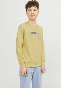 Felpa gialla con scollatura rotonda, polsini e vita a coste. Presenta il logo blu "JACK&JONES" sul davanti. Jeans in denim chiaro.