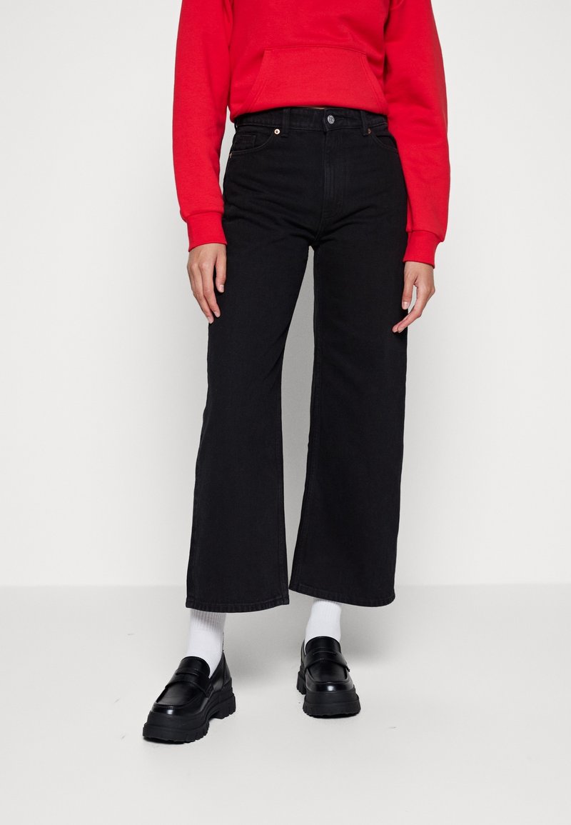 Svarta vida jeans i denim, med fem fickor och hög midja. Matchas med svarta loafers och vita strumpor.