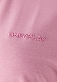 Lyserød T-shirt stof med en glat tekstur, der har et broderet "ONLY PLAY" logo i matchende tråd, placeret nær bunden.