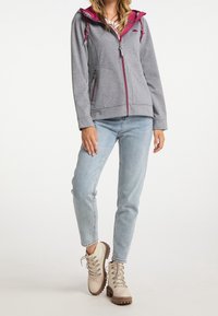 Hoodie zippé gris avec une capuche rose, doté de deux poches avant et de cordons. Associé à un jean bleu clair et des bottes beiges à lacets.