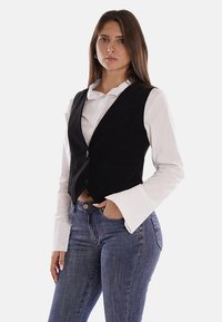 Gilet nero senza maniche con una vestibilità su misura, realizzato in un tessuto testurizzato, con chiusura a un bottone e due tasche frontali.