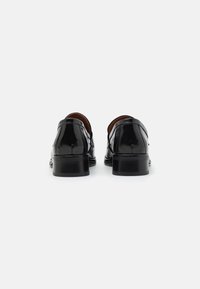 Sorte lædersko med en poleret overflade, afrundet tå, lave hæle og slip-on design, der har detaljeret syning langs sømmene.