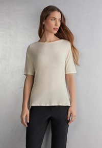 Kortærmet cremefarvet t-shirt lavet af blødt stof, med rund halsudskæring og en afslappet pasform, parret med sorte bukser.