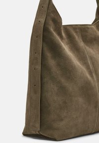 Torebka typu tote w kolorze oliwkowej zieleni, wykonana z zamszu o miękkiej teksturze, z bocznymi szwami i płaskim dnem. Uchwyty również wykonane są z zamszu, wzmocnione przeszyciem.