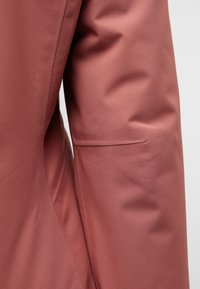 Roze stoffen materiaal met een gestructureerd oppervlak en subtiele patronen. Bevat een naaddetail en een discreet zijvakje op de mouw.