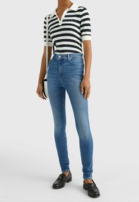 Camisa polo a rayas en azul marino y blanco con cuello; combinada con jeans ajustados azules. Los accesorios incluyen un pequeño bolso cruzado negro y mocasines negros.
