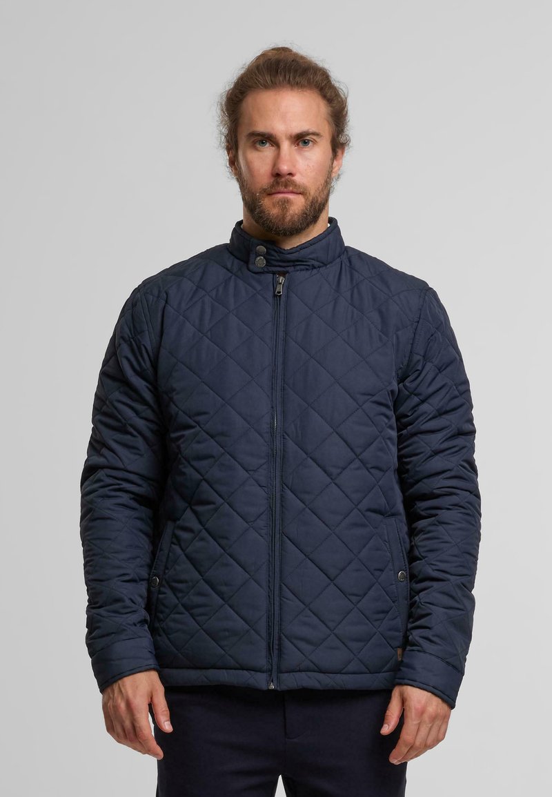 Marine blauwe gestikte jas met een staande kraag, diagonale stiksels, een voorkant rits en zijzakken. De stof is glad met een matte afwerking.